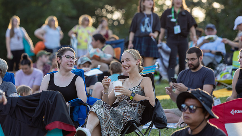 Young Friends members smiling and enjoying an outdoor concert sitting in chairs.