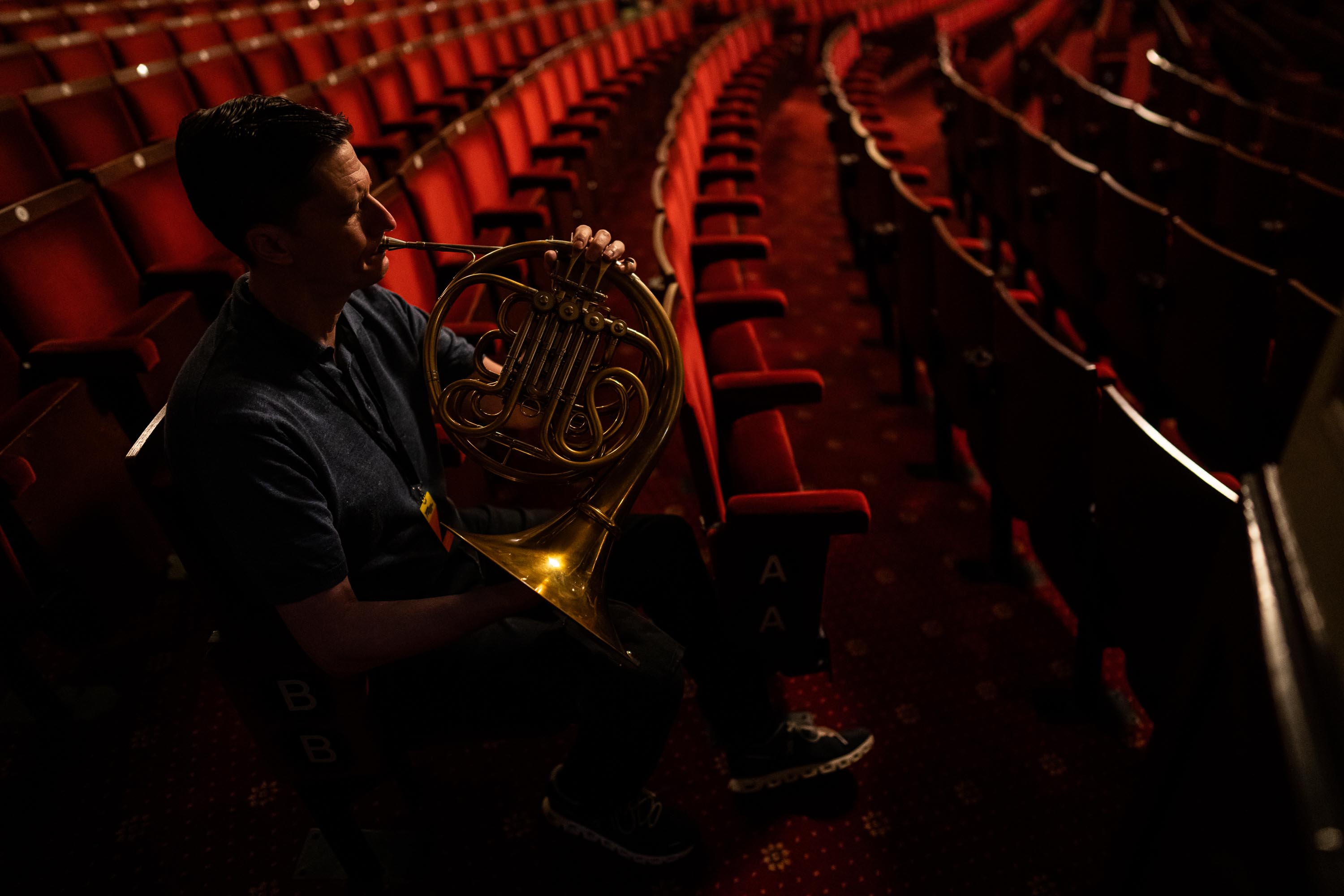 Horn player Christopher Dwyer warms up in the auditorium’s seats