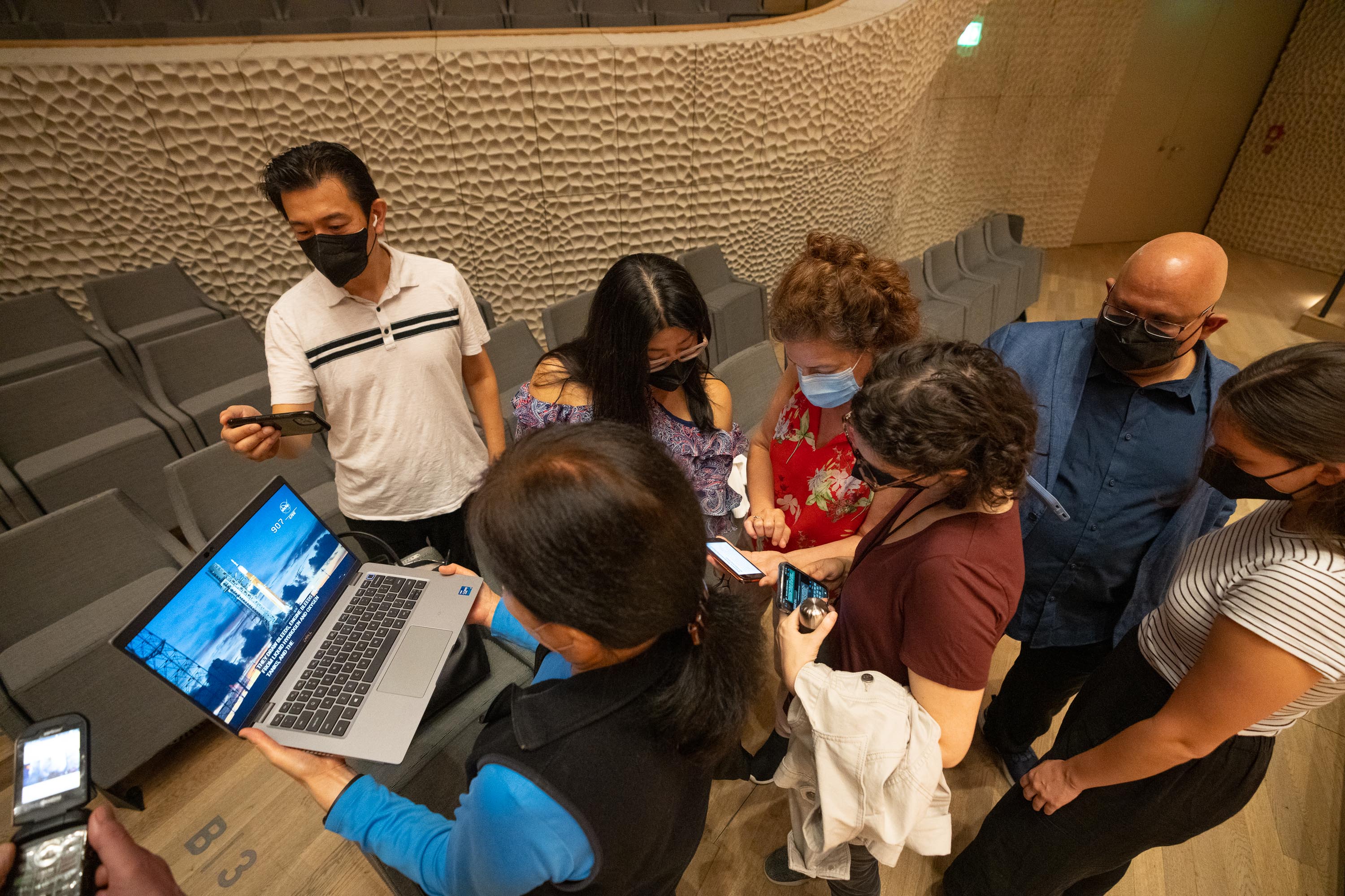 Musicians gather around phones and a laptop at the Elbphilharmonie to watch the launch of NASA’s Artemis I