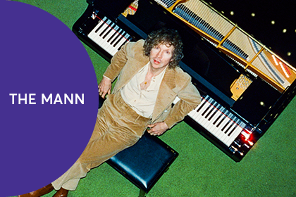 Artist Beck leaning against a piano with a purple text overlay reading, "The Mann".
