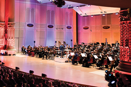 The Philadelphia Orchestra playing on stage with bright, pink lights in the background.