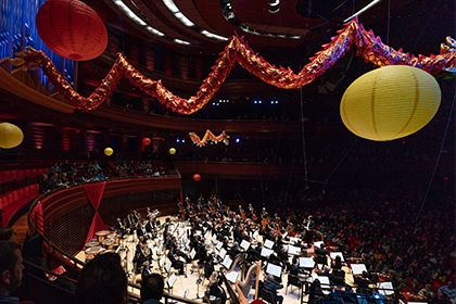 Lunar New Year key image of red, green, and gold abstract The Philadelphia Orchestra performing on stage with paper lanterns hanging above..