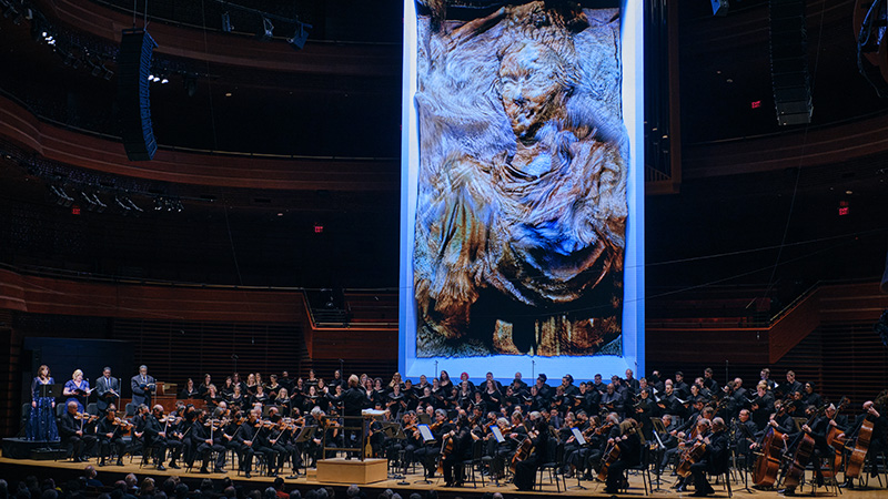 The Philadelphia Orchestra playing on stage with a large projected graphic behind.